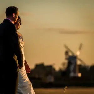 Bride and groom looing toward Cley Windmill at dusk.